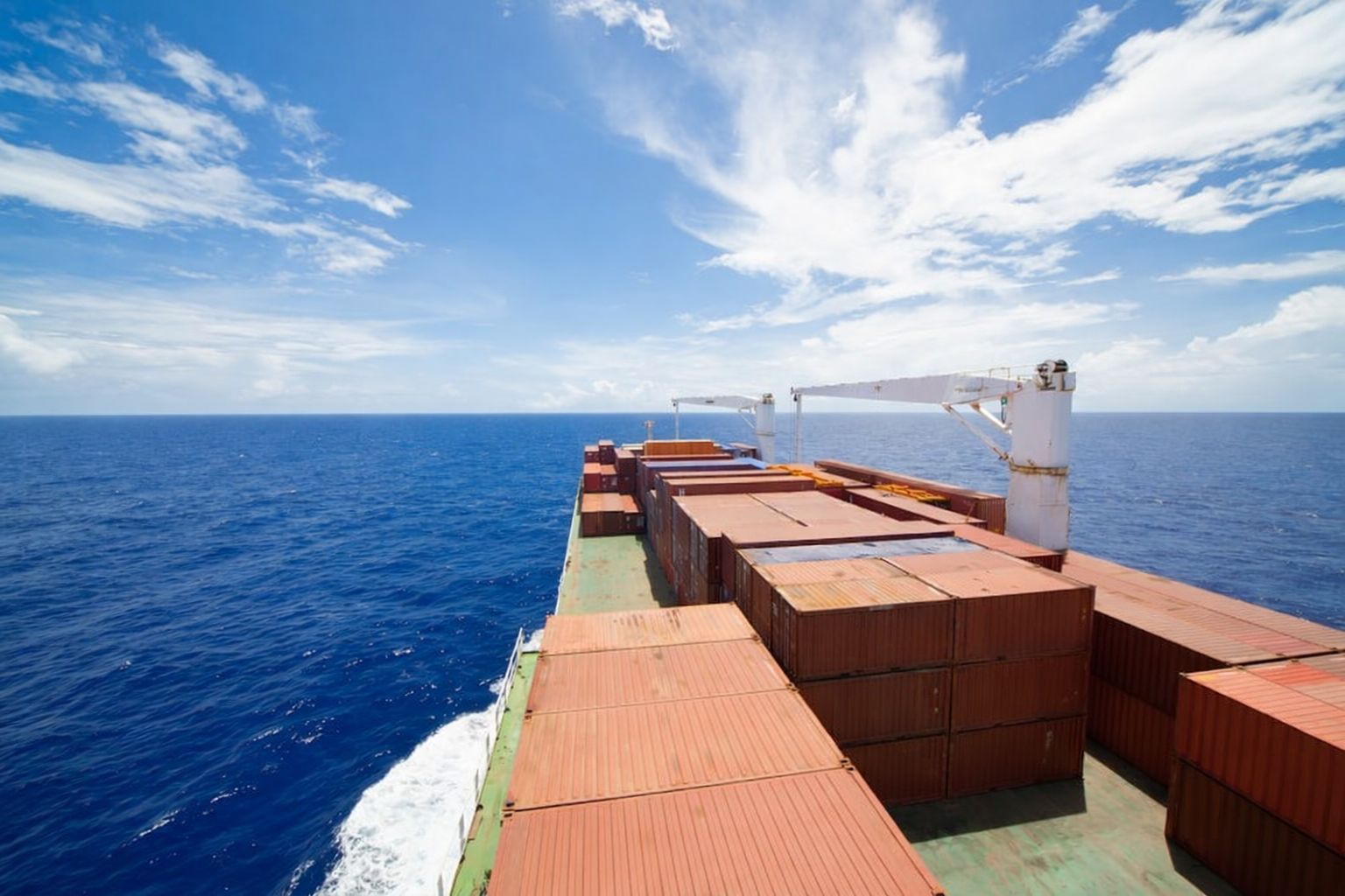 Frachtschiff beladen mit Containern auf dem weiten Meer unter blauem Himmel.