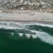 Luftaufnahme brechender Wellen vor einem breiten Stadtstrand