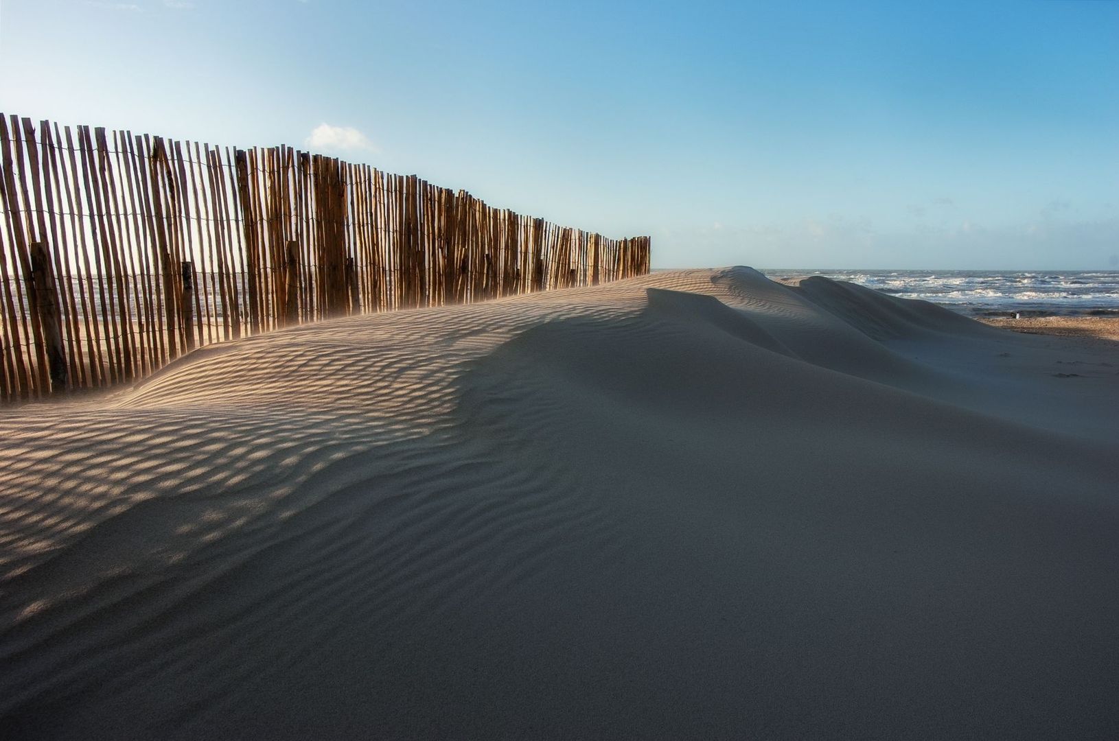 Holzzaun stabilisiert eine Sanddüne am windigen Meeresstrand