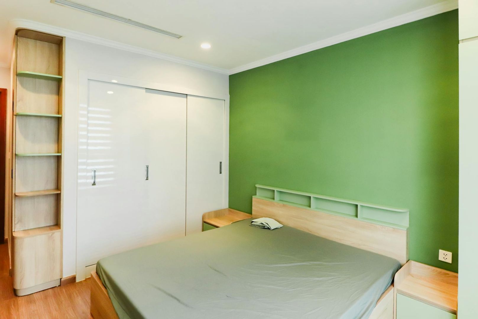 Schlafzimmer in Ferienwohnung mit grüner Wand und weißem Schrank.